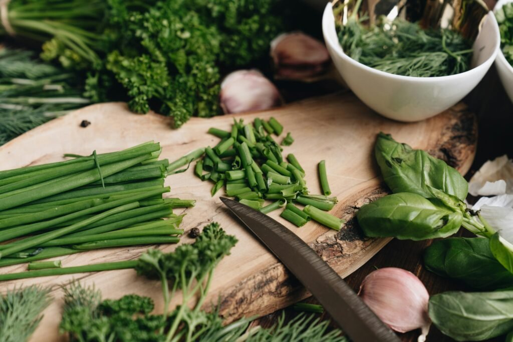 Fresh seasonal greens and herbs being chopped on a wooden board, highlighting the importance of seasonal vegetables in Ayurvedic nutrition for strength.
