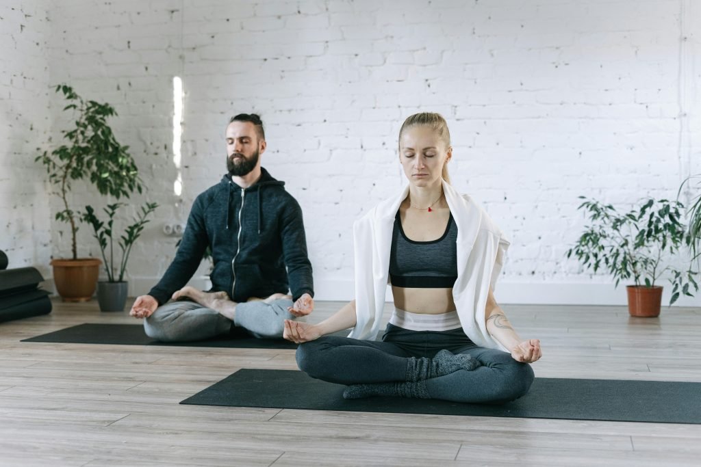 A man and woman meditating in lotus pose on yoga mats, demonstrating a peaceful morning routine for good health.