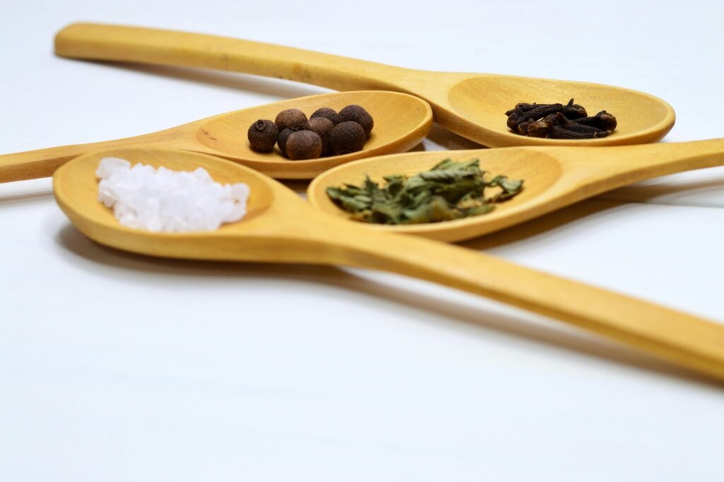 Four wooden spoons holding warming Ayurvedic spices like cloves and allspice, used to boost digestive (agni) fire and immunity in winter.